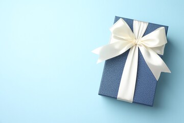 Gift box with beautiful bow on light blue background, top view. Space for text