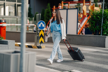 Businesswoman walking with suitcase and water bottle on pedestrian crossing