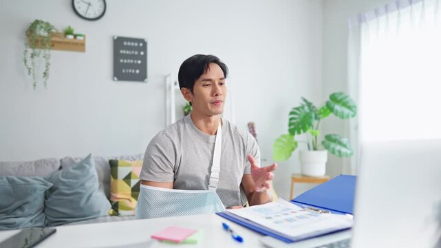 Injured Asian businessman wearing hand splint while working from home. 