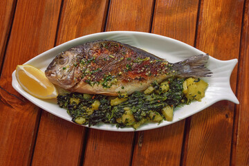 Balkan cuisine. Grilled fish of  sea bream with green leafy vegetables. Rustic table. Copy space