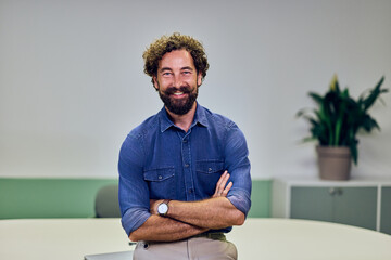 Smiling Man in Casual Attire Standing with Arms Crossed in Bright Office