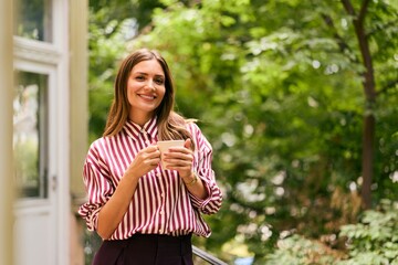 Smiling Woman Outdoors Holding Coffee Mug Amidst Lush Greenery