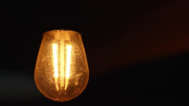 Warm glowing led filament light bulb illuminating dark surroundings, creating intimate ambiance with soft, inviting luminescence against deep shadow background