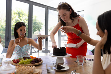 Cutting chocolate cake, young woman in red dress celebrates birthday with friends