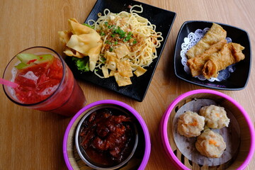 Variety of dim sum dishes including siomai, chicken feet, tofu skin, noodles, and iced drink served together on a wooden table.  
