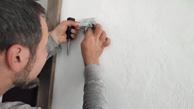 Bearded male electrician installs socket and switch, makes repairs. Safety when working with electricity