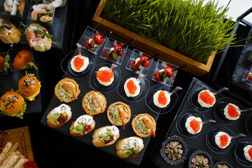 Mini burgers with sesame and shrimp tartlets on a black tray.