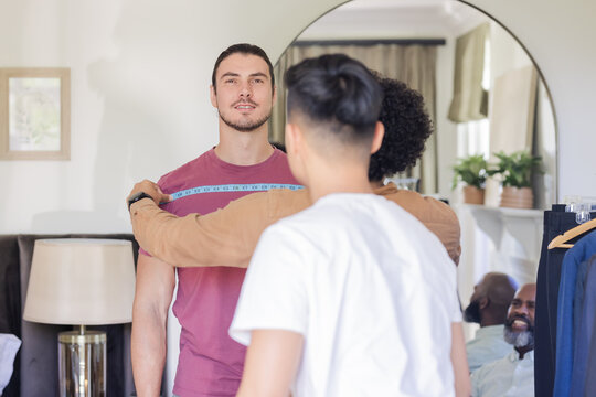 Groom getting measured for suit fitting, surrounded by friends, smiling warmly