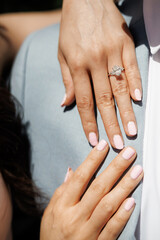 Close-up of female hands with elegant pink manicure and a sparkling diamond engagement ring. Woman put her hands on man's shoulder symbolizing love, commitment and romantic relationships
