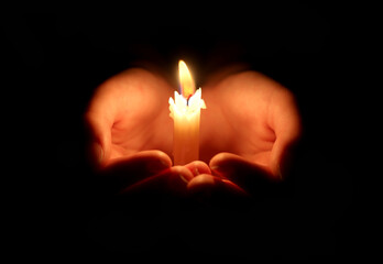 burning candle and hands protect the flame so that it does not go out. Black background. Space for...