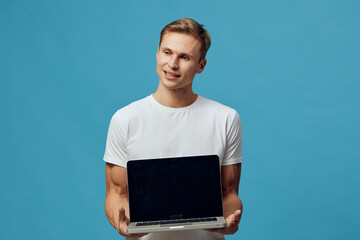 Smiling young man holding open laptop computer isolated on blue background studio portrait. People lifestyle concept