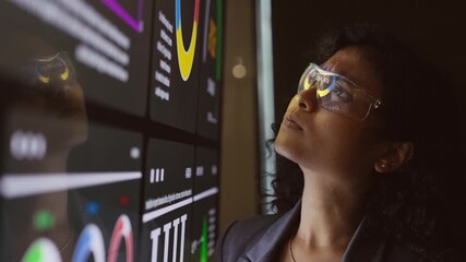 Analyst reviews colorful data dashboards on large digital screen in modern tech workspace. Scene reflects analytics, technology, research, metrics, insight, strategy, and data-driven analysis. - Powered by Adobe