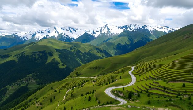 Aerial view of a winding road traversing lush green hills towards snow-capped mountain peaks under a cloudy sky. - Powered by Adobe