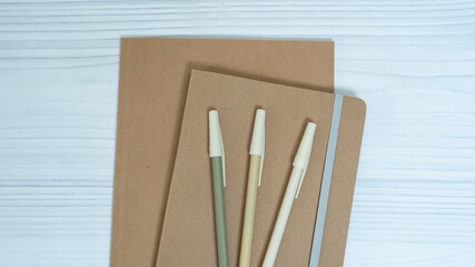 Minimalist sustainable stationery set with kraft notebooks and pencil on white wooden background.