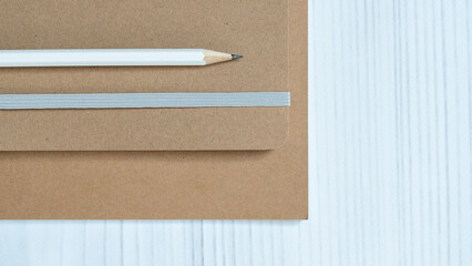 Minimalist sustainable stationery set with kraft notebooks and pencil on white wooden background.