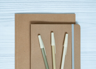 Minimalist sustainable stationery set with kraft notebooks and pencil on white wooden background.