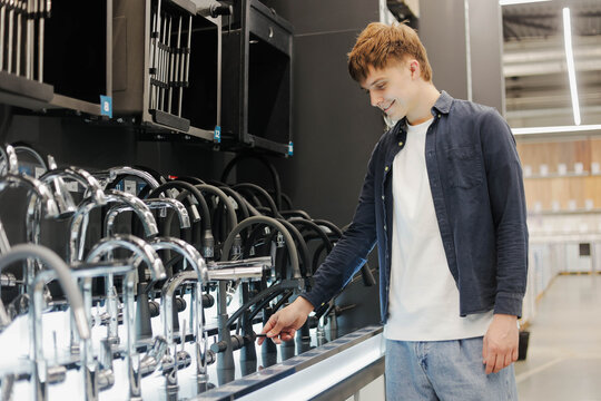 Young male customer choosing new sink faucet for his home at hardware store or shopping mall