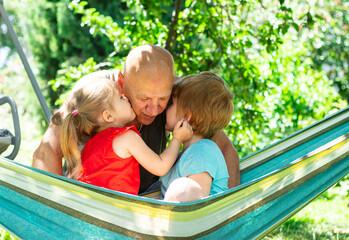 Cheerful family, grandchildren kissing and hugging grandfather and relaxing outside in summer nature