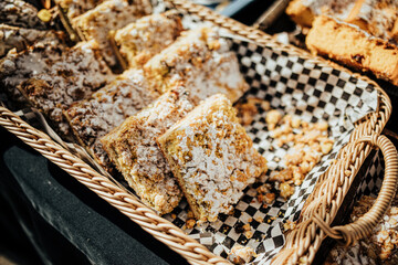 An assortment of pastries, muffins, and baked goods displayed in baskets and trays at an outdoor market stall, sprinkled with sugar and nuts for a rustic treat