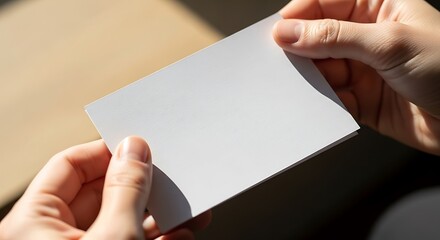 Hands holding a blank white paper sheet in bright natural daylight