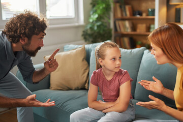 Parents engage in a serious discussion in the living room while their daughter looks worried and...