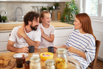 A joyful family shares a delightful breakfast at their cozy kitchen table, where laughter echoes as they enjoy each other's company and delicious food in a sunny setting.