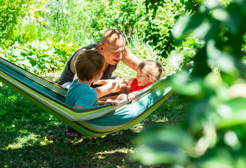 Cheerful family grandfather and grandchildren relaxing outside in the park, kids sitting in the hammock 