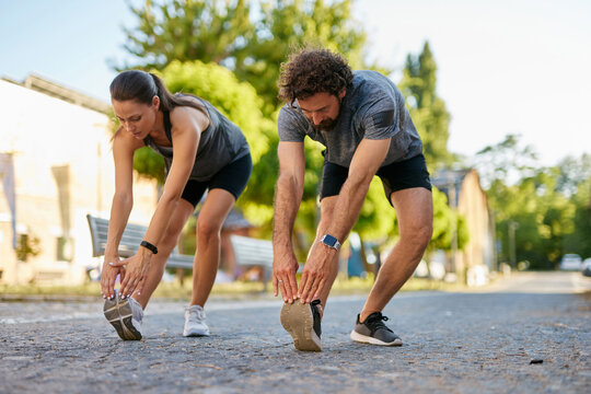 Two individuals perform stretching exercises on a peaceful street in the morning light, emphasizing a healthy lifestyle and the importance of physical activity in daily routines.