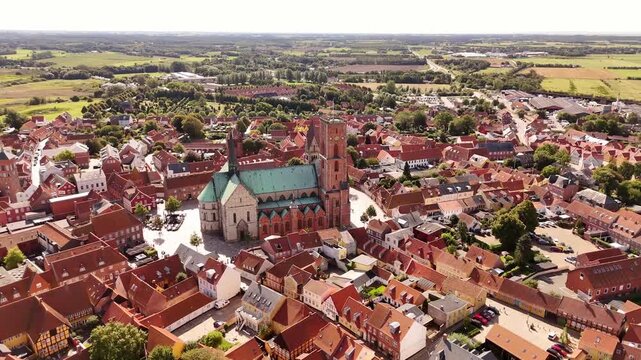 Aerial view of Ribe Cathedral, its green roof contrasting with the red rooftops of surrounding buildings and lush green landscape, Ribe, Denmark.