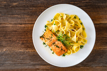 Pasta with baked salmon steak on wooden table	