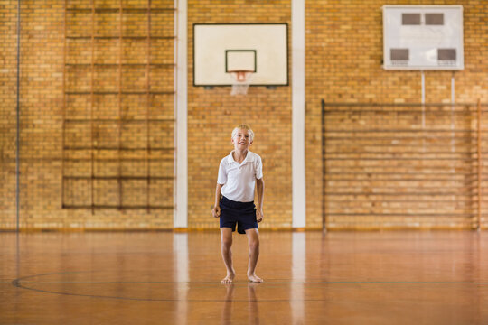 Fototapeta Barefoot boy wearing white polo and shorts standing in gym with basketball hoop and climbing frame