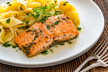 Pasta with baked salmon steak on wooden table	
