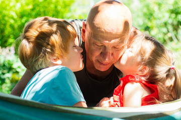 Happy family, cute children kissing grandfather and relaxing outside in the summer park