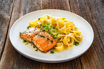 Pasta with baked salmon steak on wooden table	