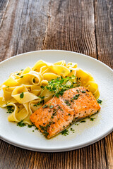 Pasta with baked salmon steak on wooden table	