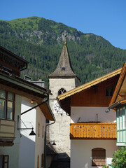 Historic Clock Tower In Canazei Village Amidst Alpine Buildings and Mountain Background, Italy