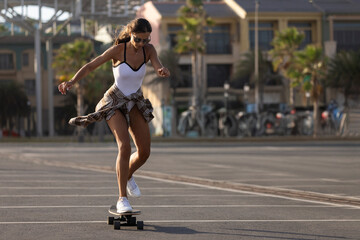 Fototapeta premium Skater girl in plaid shirts and swimsuits laughing and walking with skateboard at skate park. The summer solchechny frame.