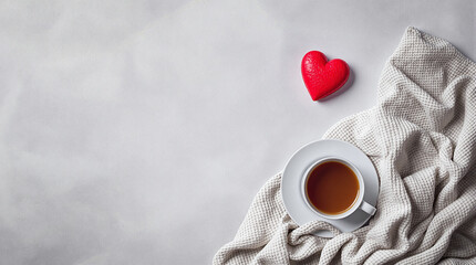 Cozy flat lay with red heart, warm tea cup, and soft blanket on a light background