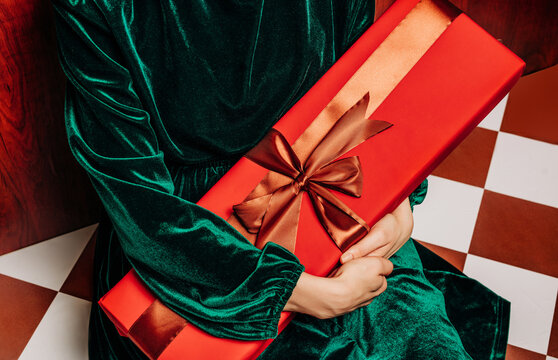 Stylish woman in green dress holding a red Christmas gift box indoors