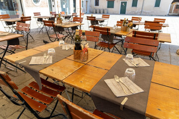 Empty outdoor restaurant tables in sunny square. Neatly set wooden tables and chairs at an outdoor restaurant in a quiet European square, ready for customers on a sunny day.