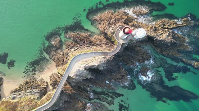 Aerial view of the Pointe du Minou lighthouse, a white tower with a red top, sitting on rocky cliffs surrounded by turquoise water, Plouzan&eacute;, France.