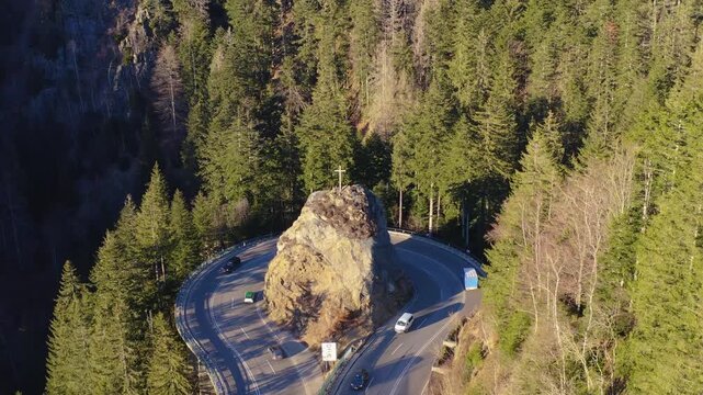 Aerial view of the winding road curves around a striking rock formation topped with a cross, surrounded by lush, dense forest, Breitnau, Baden-W&uuml;rttemberg, Germany.