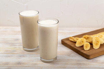 Banana milkshake. Refreshing banana smoothie is presented in tall glasses, showcasing creamy texture, alongside sliced bananas arranged on wooden board, creating appetizing scene. Banana smoothie