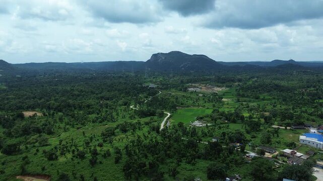 Aerial view of vibrant green landscape with a winding road and a mountain in the background, contrasting with a cloudy sky, Bundu, Jharkhand, India.
