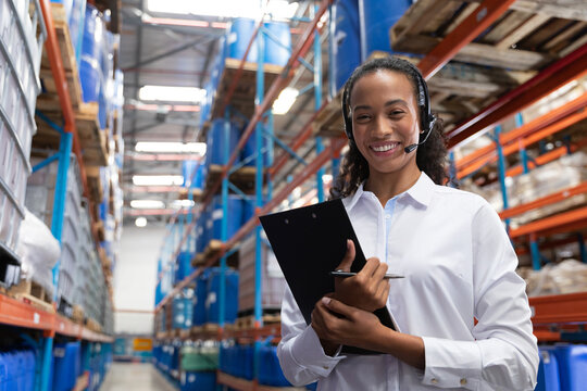 Warehouse manager wearing headset and holding clipboard and pen inspecting blue bins in aisle