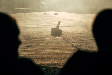 Golden light, smoke, and silhouettes of spectators create a dramatic scene at a drift show, with...