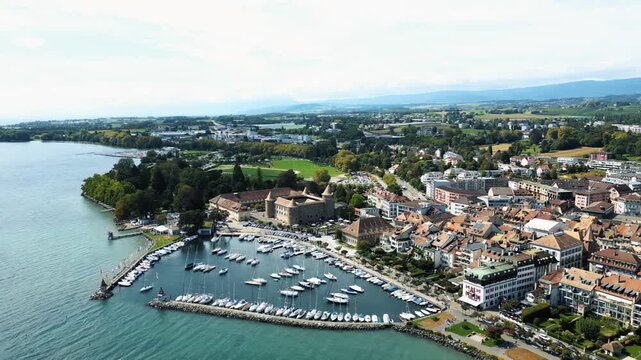 Aerial view of Morges Castle juxtaposed against a harbor filled with boats, with the town's terracotta rooftops cascading towards the serene lake, Morges, Vaud, Switzerland.