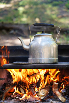 Brewing tea or coffee in a metal teapot over a campfire in nature.
