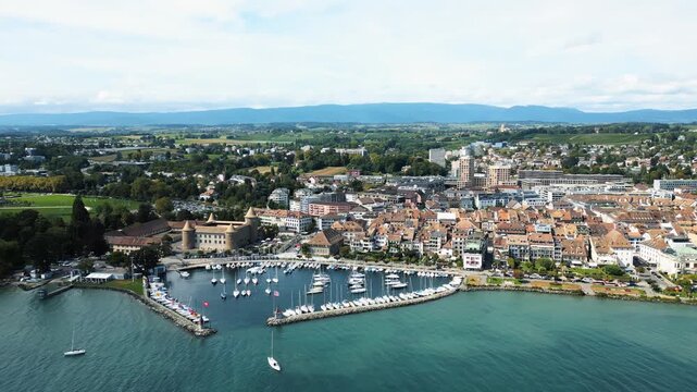 Aerial view of Morges Castle and a vibrant harbor filled with white sailboats against the blue water, contrasting with the red-roofed buildings, Morges, Vaud, Switzerland.