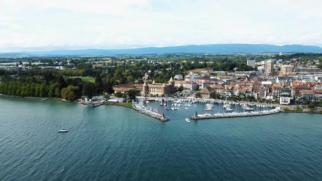 Aerial view of Morges Castle and harbor featuring sailboats contrasting with the town's terracotta rooftops and the lake's turquoise waters, Morges, Vaud, Switzerland.